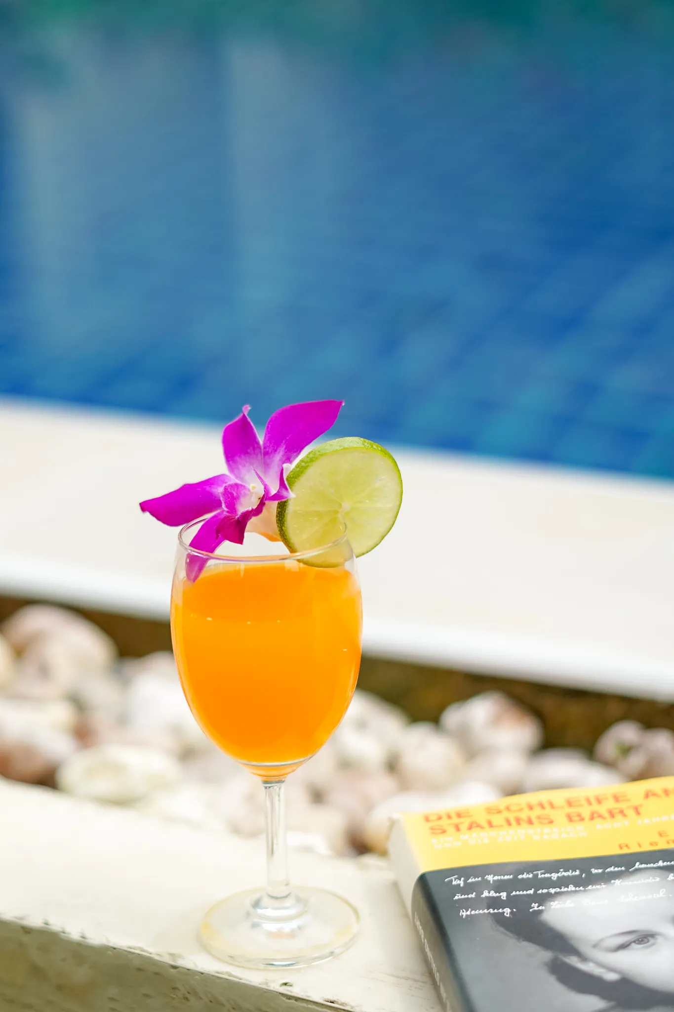 A glass of orange juice beside a swimming pool